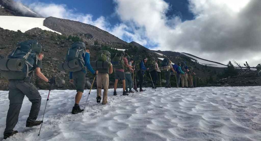 a group of backpacking students hike across a snowy field on an outward bound course
